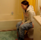 A girl is video-recorded by her friend as she sings and takes a shit while sitting on a toilet. We assume her pain and breakup is with her own poop leaving her asshole. There is an audible plop sound, and she has some singing talent as well.